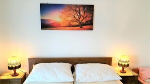 A double bed with white bedding, two bedside lamps, and a wall-mounted picture of a sunset. - Charming Apartment by Worthersee (Techelsberg am Worther See)