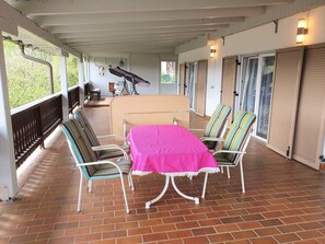 A covered patio area with a table and chairs, a bench, and a view of the outdoors. - Charming Apartment by Worthersee (Techelsberg am Worther See)