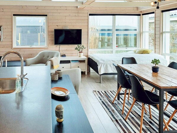 A modern, well-lit room with a large bed, a dining table, and a TV mounted on the wall.