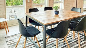 A wooden dining table with six black chairs, a potted plant, and large windows with a view of greenery outside. - 6 Person Holiday Home in Karrebaeksminde (Karrebæksminde)