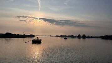 A calm body of water with a small boat anchored in the center, surrounded by a calm sky with a visible contrail.