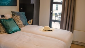 Uma cama de casal com lençóis brancos, almofadas verde-água e brancas, e um chapéu de palha sobre a cama.