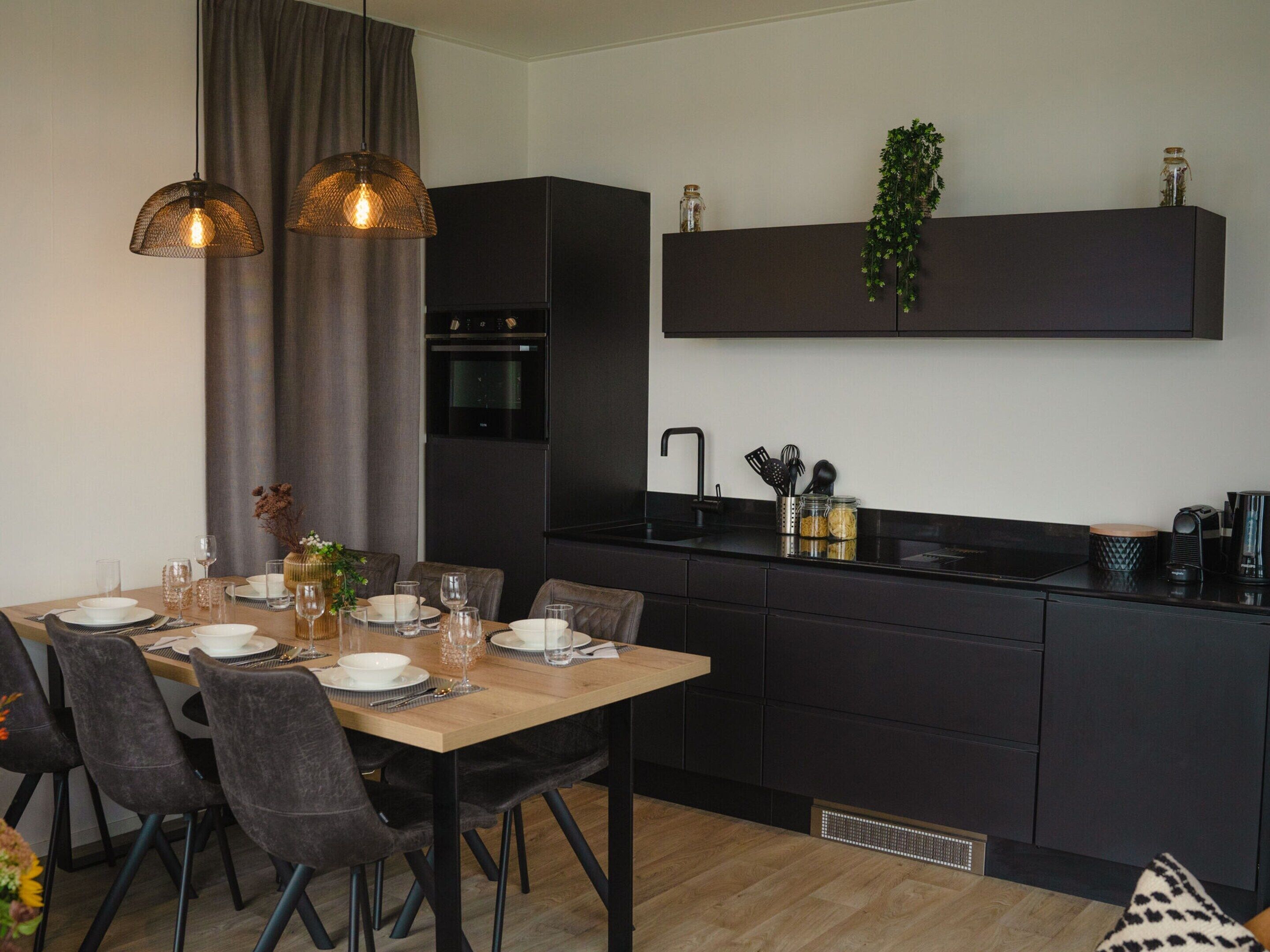 Eine moderne Küche mit dunklen Schränken, einem Holztisch und Pendelleuchten.