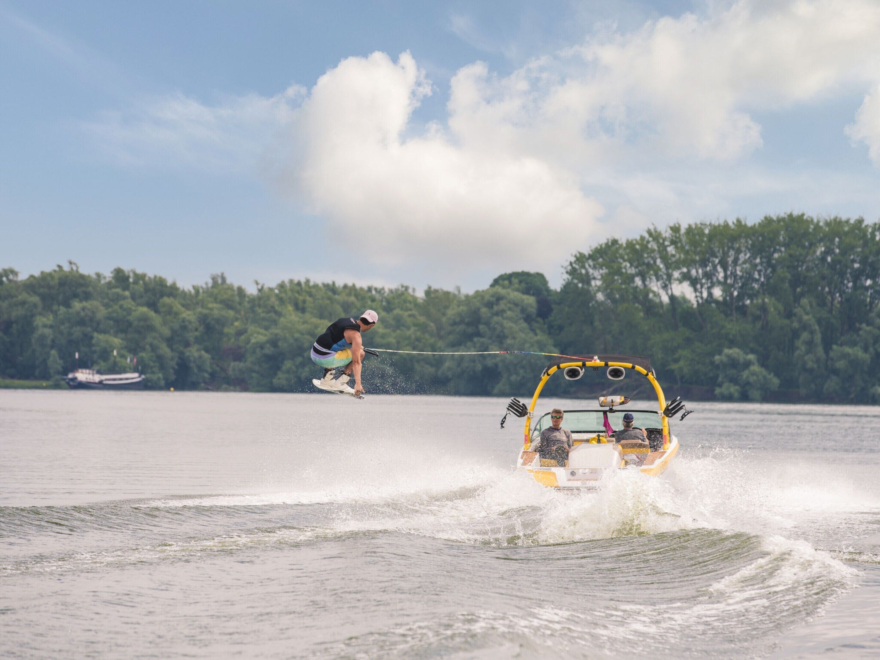 A wakeboarding event with a wakeboarder performing a jump and a boat towing them.