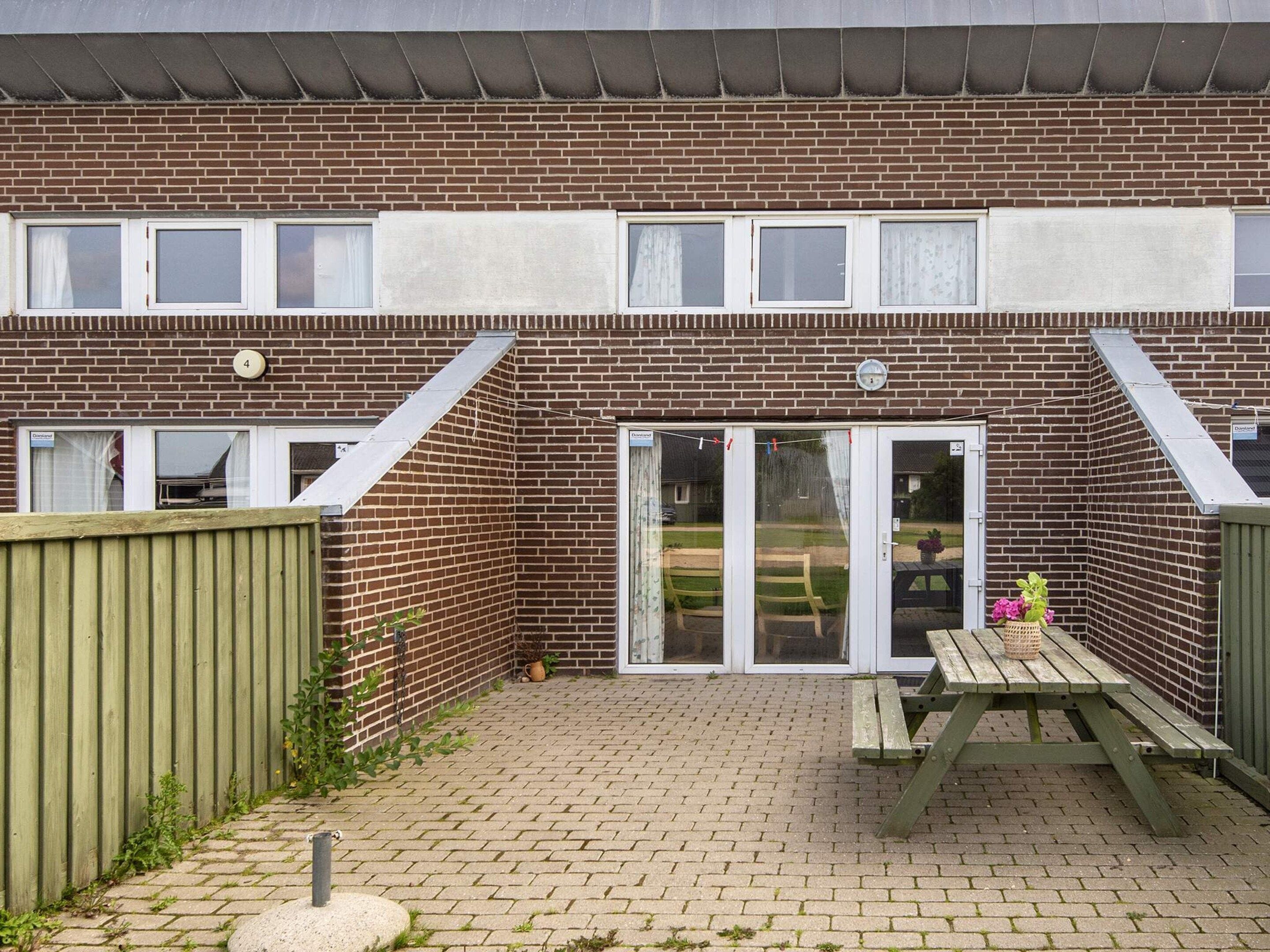 A brick building with a patio area, a wooden fence, and a picnic table.