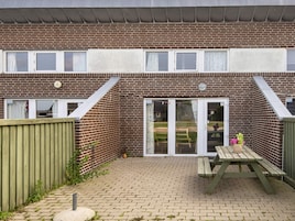 A brick building with a patio area, a wooden fence, and a picnic table.