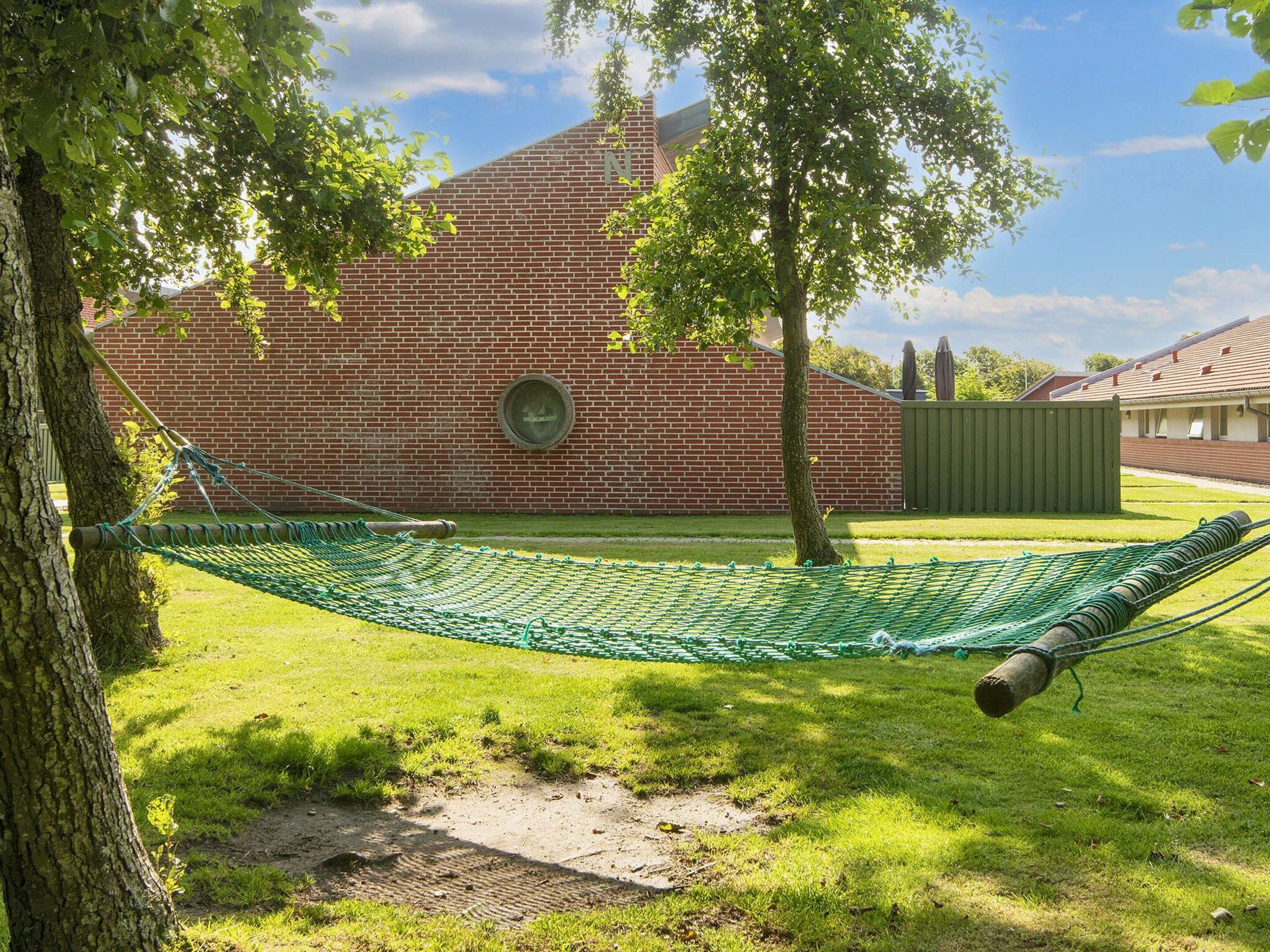 A brick building with a circular window, a hammock, and a tree in a grassy yard.