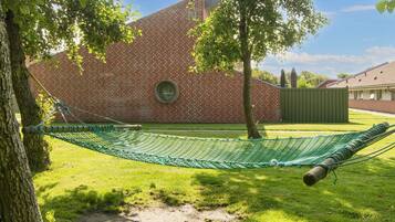 A brick building with a circular window, a hammock, and a tree in a grassy yard.