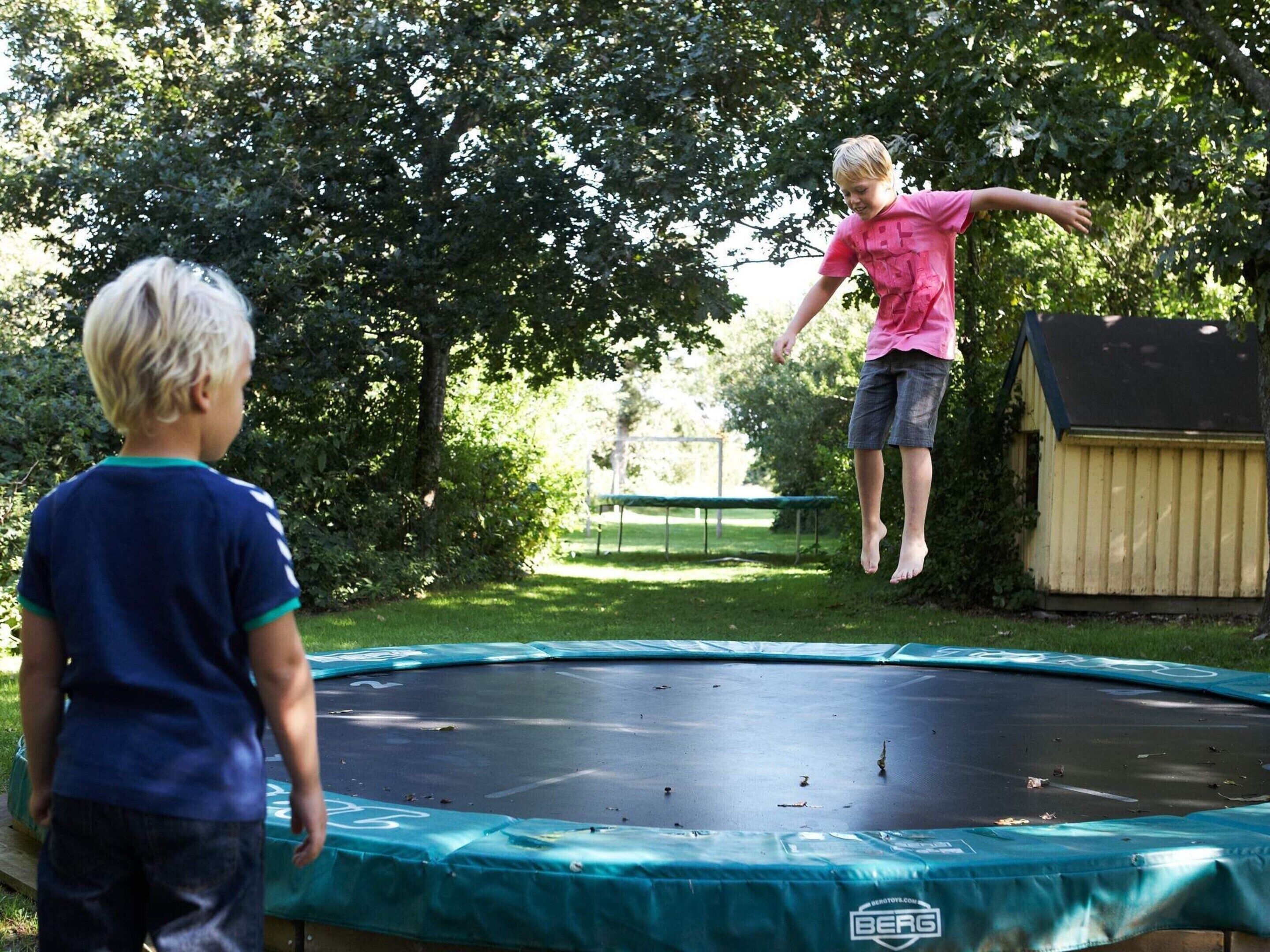 A trampoline in a backyard with a wooden shed and trees in the background.