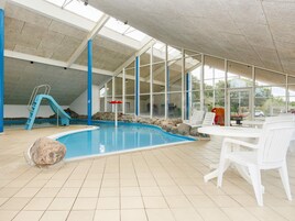 Una piscina interior con tobogán, sillas de descanso y vistas al exterior.