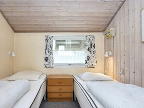 Um quarto pequeno e acolhedor, com duas camas de solteiro, uma cômoda de madeira e uma janela com cortinas florais.