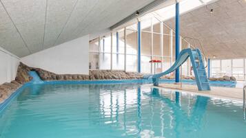 An indoor swimming pool with a blue slide, stone walls, and large windows.