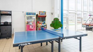 Ein Tischtennistisch mit blauem Netz, umgeben von Spielautomaten und einem großen Fenster.