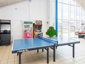 Ein Tischtennistisch mit blauem Netz, umgeben von Spielautomaten und einem großen Fenster.