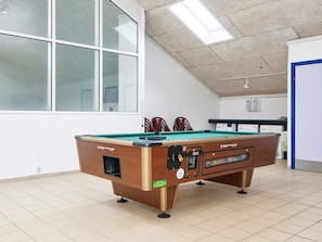 Ein Billardtisch in einem Raum mit großen Fenstern, einem Deckenventilator und einer Tür.