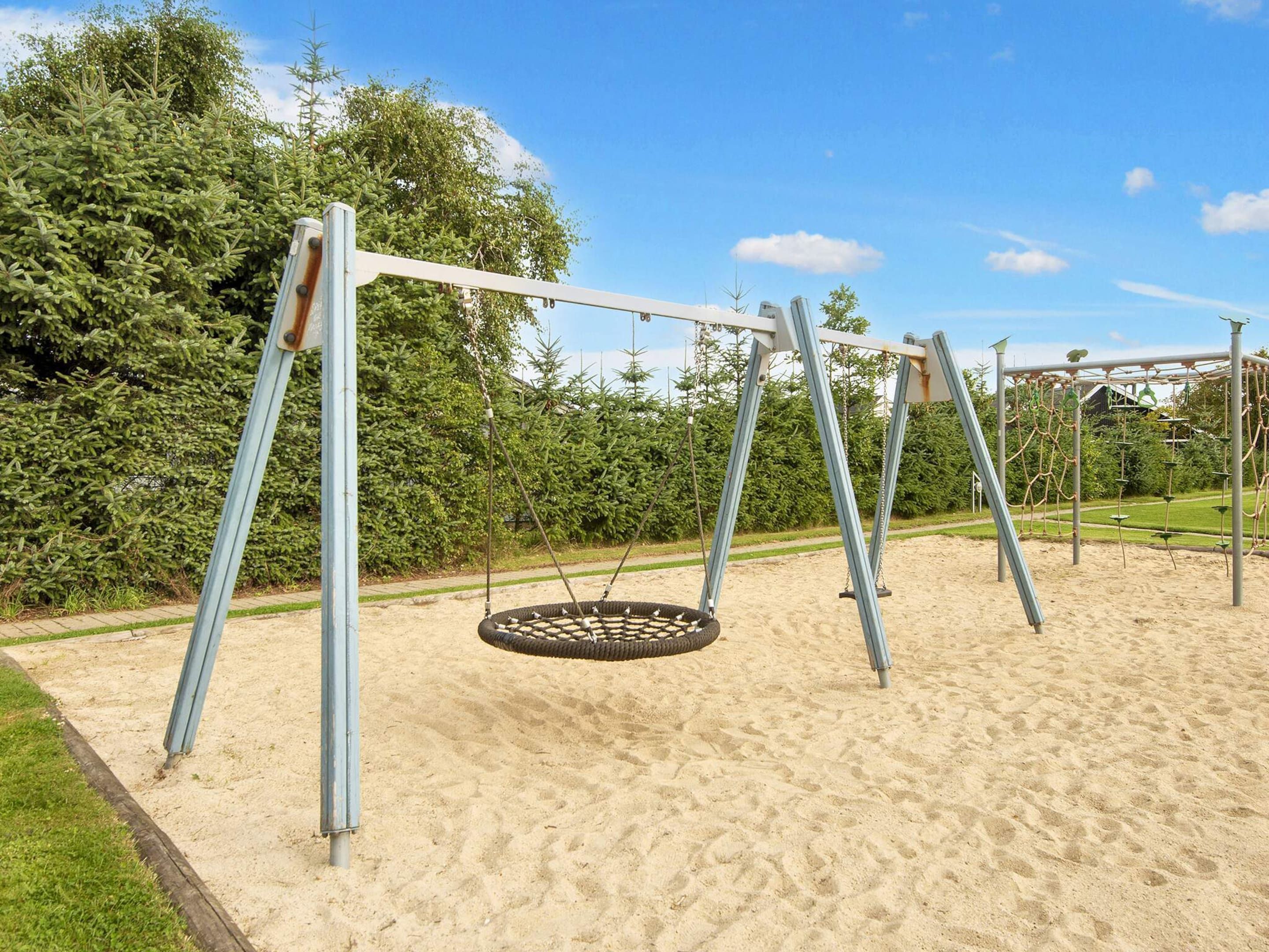 A playground with a swing set and tire swing, surrounded by sand and greenery.