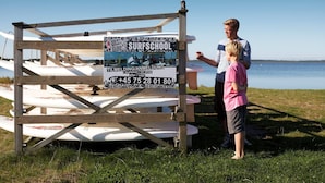 Una estructura de madera con un letrero que anuncia una escuela de surf, rodeada de tablas de surf.