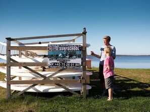 Eine Holzhütte mit einem Schild, das eine Surfschule bewirbt, umgeben von Surfbrettern.