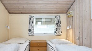 Ein kleines, gemütliches Zimmer mit zwei Einzelbetten, einem Holzschrank und einem Fenster mit blumigen Vorhängen.