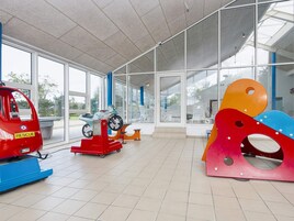 Amplio espacio interior con grandes ventanales, un vehículo de rescate rojo y esculturas abstractas coloridas.