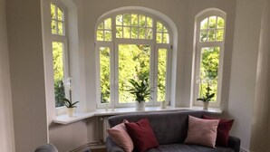 Un salon avec un canapé gris, une table basse et trois fenêtres en arc donnant sur un espace verdoyant.