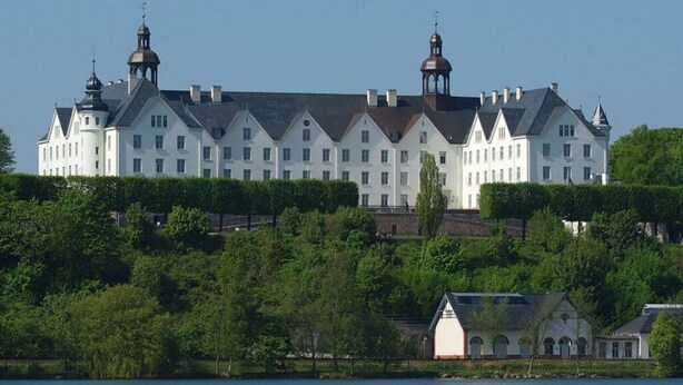 Un grand bâtiment blanc à plusieurs étages, doté d’une façade symétrique, avec une tour centrale et deux tours plus petites de chaque côté.