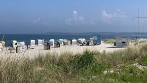 Une plage avec des cabanes de plage numérotées et, au fond, une petite construction qui ressemble probablement à un poste de surveillance des sauveteurs.