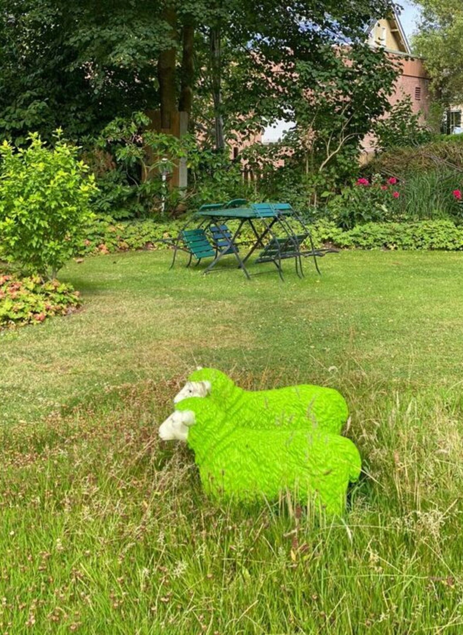 A grassy area with a green table and chairs, surrounded by trees and bushes.