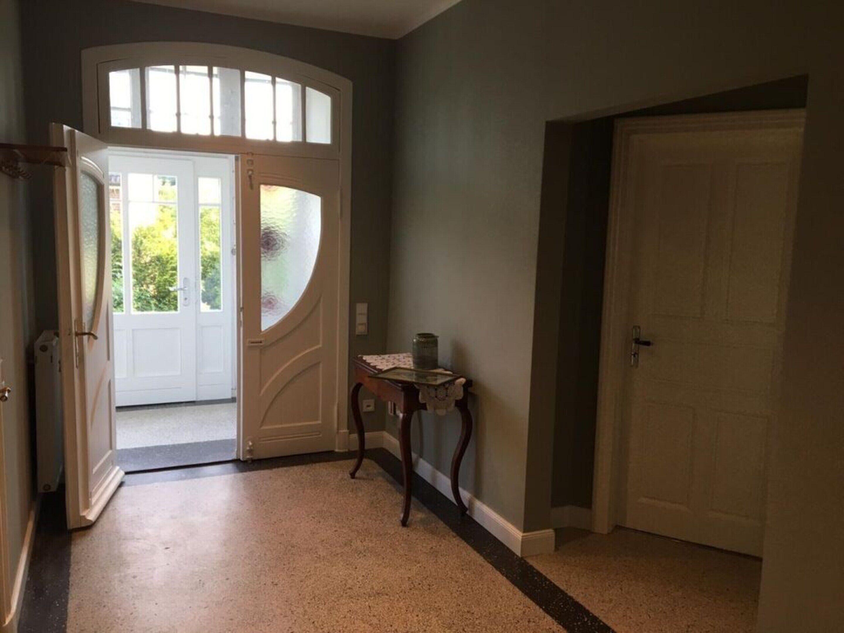 A hallway with a white door, a glass door leading outside, and a small table with a vase.