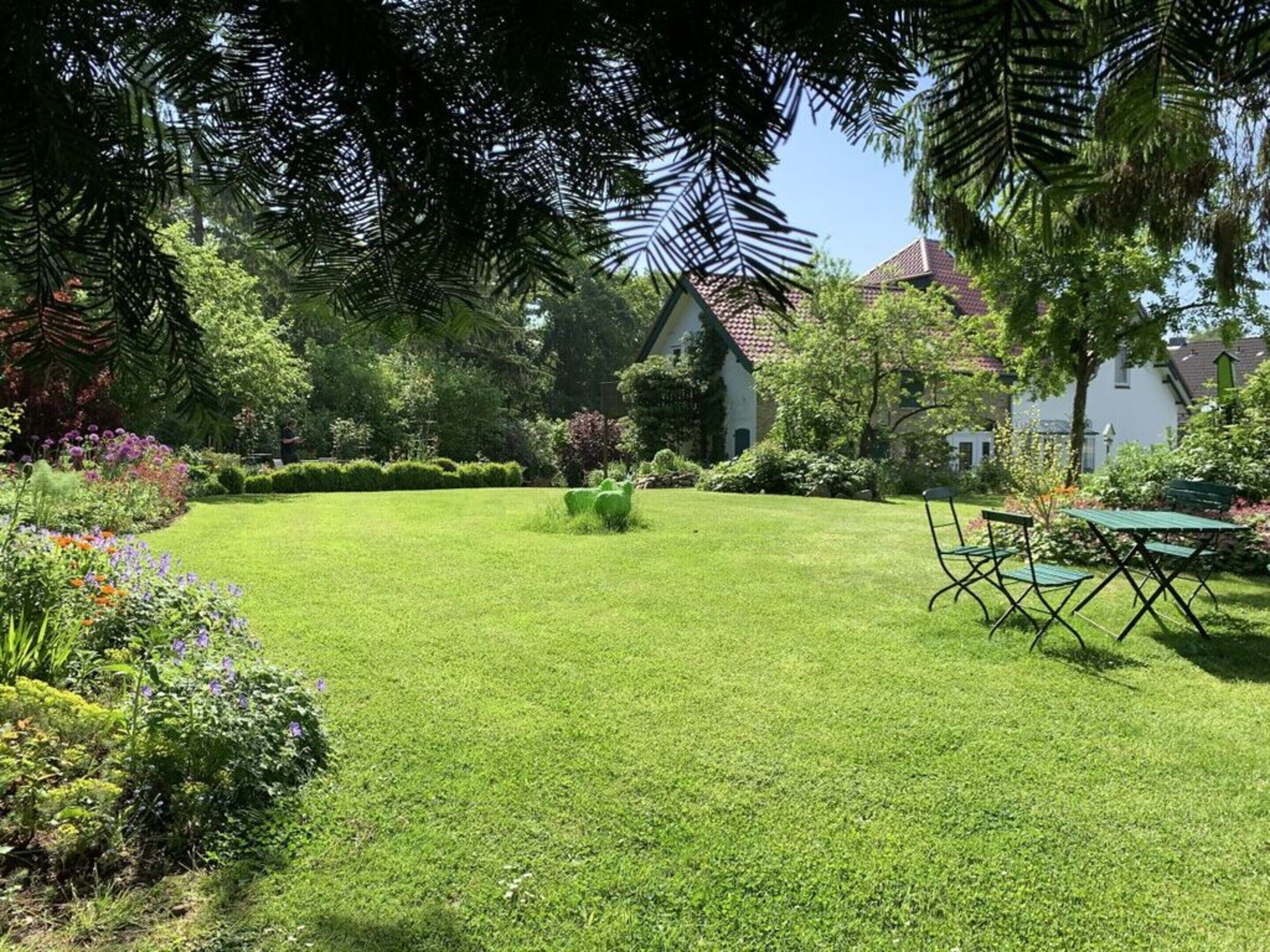 Un jardin bien entretenu, avec une pelouse, une petite table et des chaises, et un bâtiment avec un toit recouvert de tuiles rouges en arrière-plan.