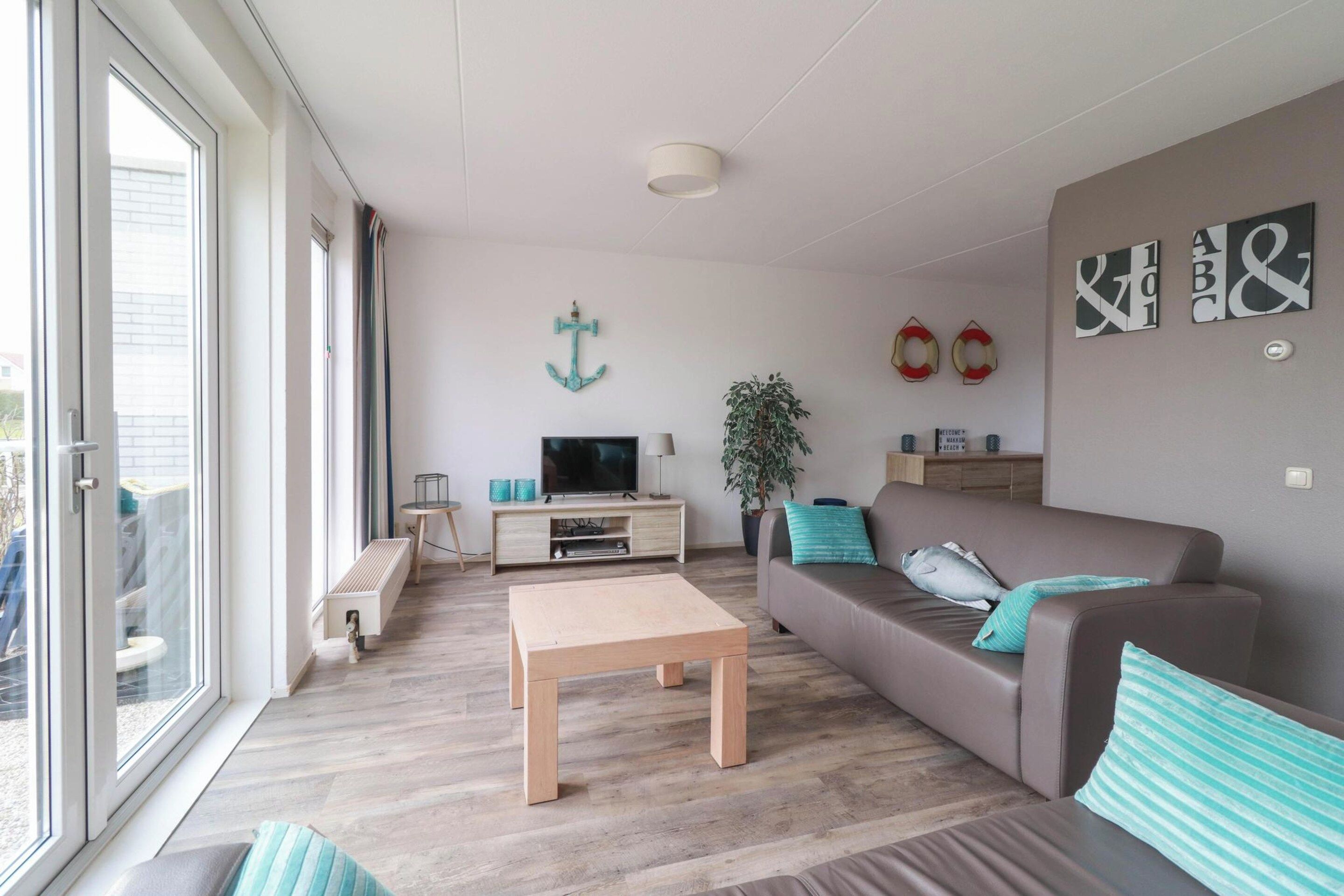 Uma sala de estar moderna com sofá, mesa de centro, TV e uma janela grande.