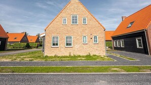A two-story house with a steeply pitched roof, multiple windows, and a visible chimney. - Cozy Holiday Home in a Holiday Park in Zeeland (Ossenisse)