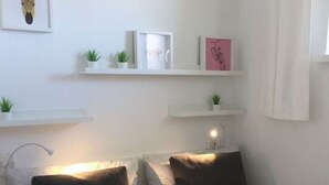 A bedroom with two beds, white walls, and shelves with plants and books. - Apartment Holiday Harbor (Grossenbrode)