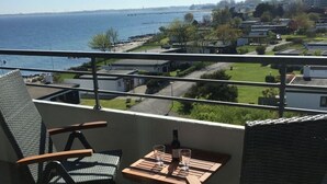 A balcony with a view of the sea and a bridge, a table with a bottle and glasses, and a chair. - Apartment Holiday Harbor (Grossenbrode)