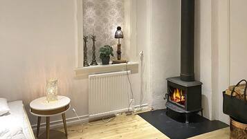 A cozy room with a fireplace, a window with curtains, a radiator, and a small table with a lamp.