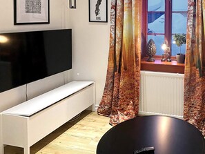A modern living room with a flat-screen TV mounted on the wall, a white bench, and a window with curtains. - 5 Person Holiday Home in Idre (Idre)