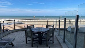 A patio with a round table and chairs, overlooking a beach with sailboats. - Apartment in Nieuwpoort With sea View (Nieuwpoort)