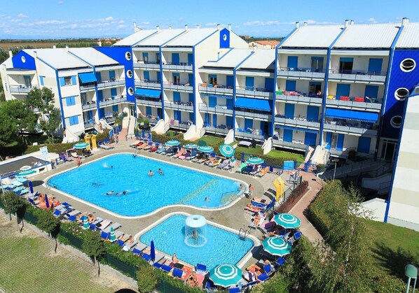 A hotel with multiple balconies, a swimming pool, and sun loungers. - Family Apartment in Caorle Near the Beach (Caorle)