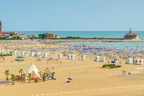 Une plage avec de nombreux parasols et des vacanciers, une aire de jeux et, au loin, un bâtiment historique.