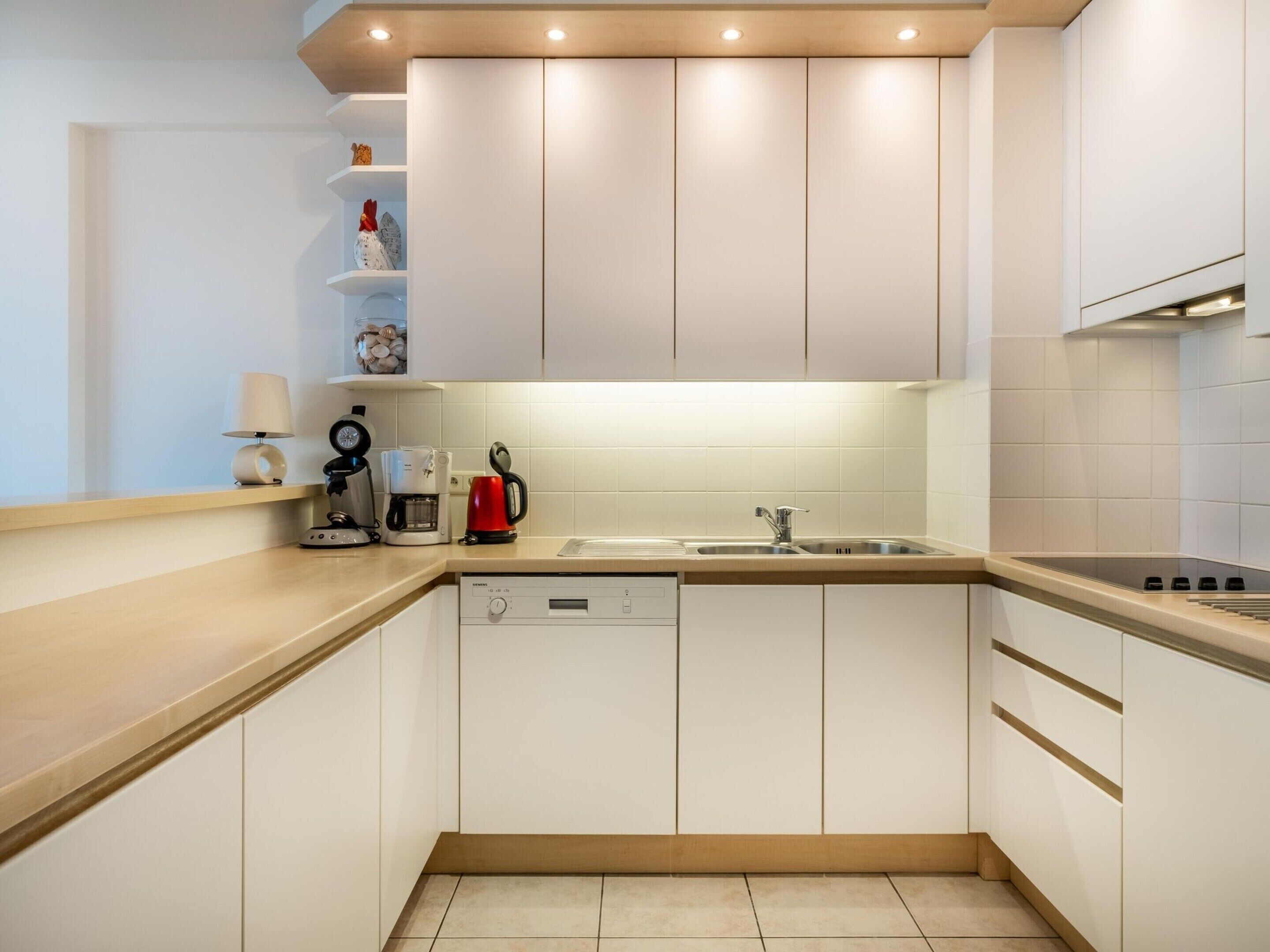 A modern kitchen with white cabinets, a built-in dishwasher, a sink, and a coffee maker.