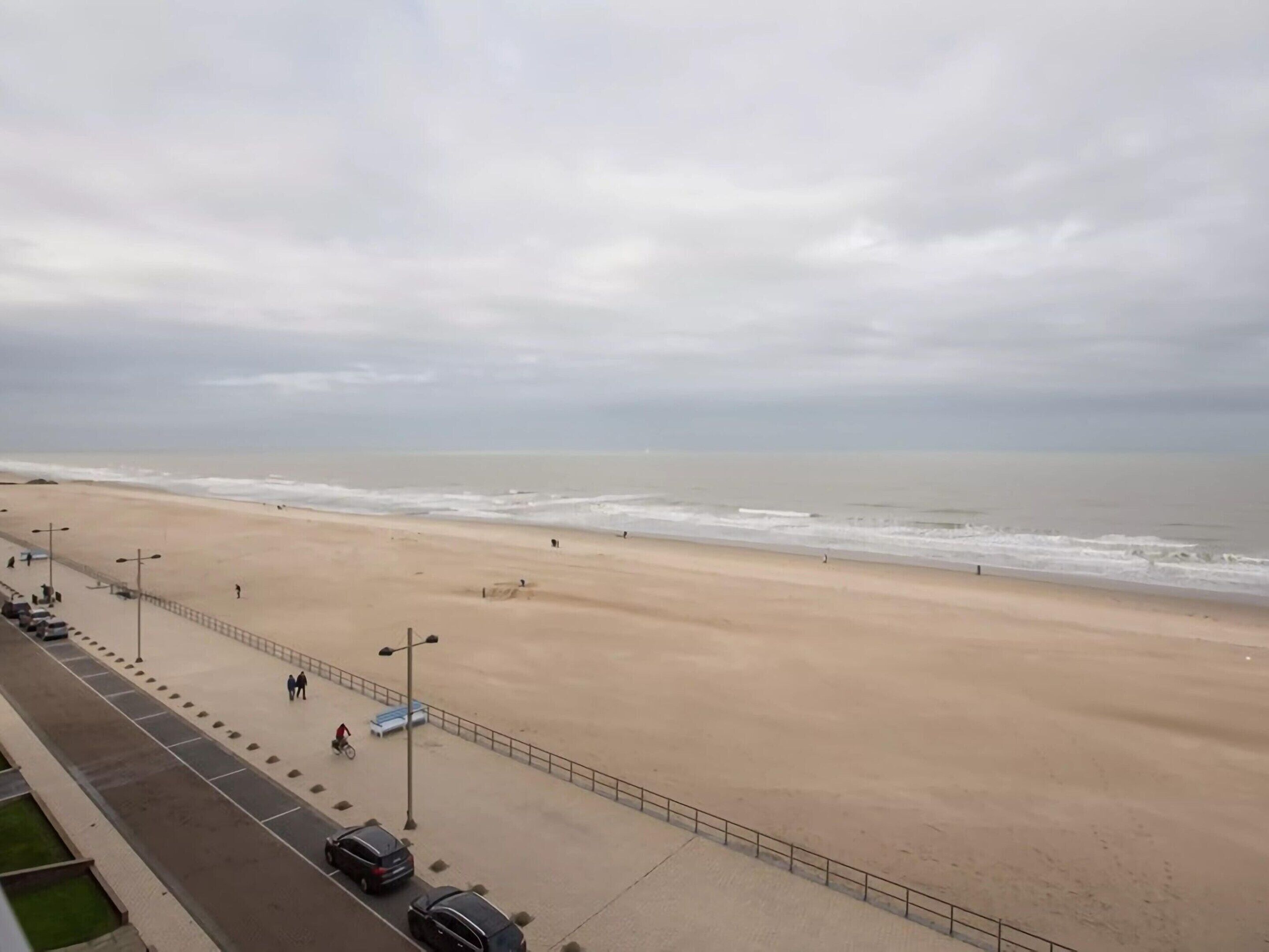 A beach with a paved walkway and parked cars.