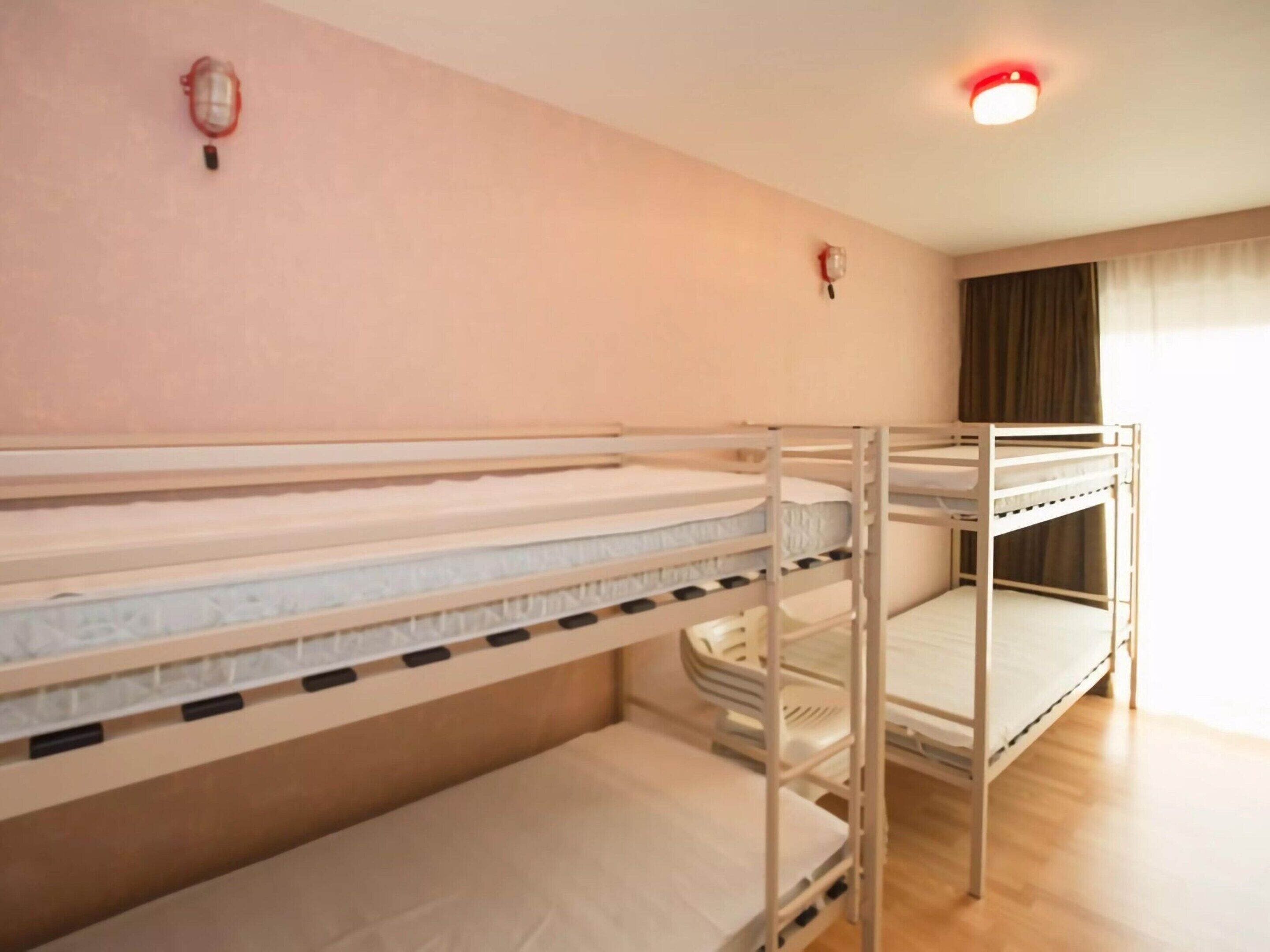 A bunk bed room with a light pink wall, a ceiling light, and a window with curtains.