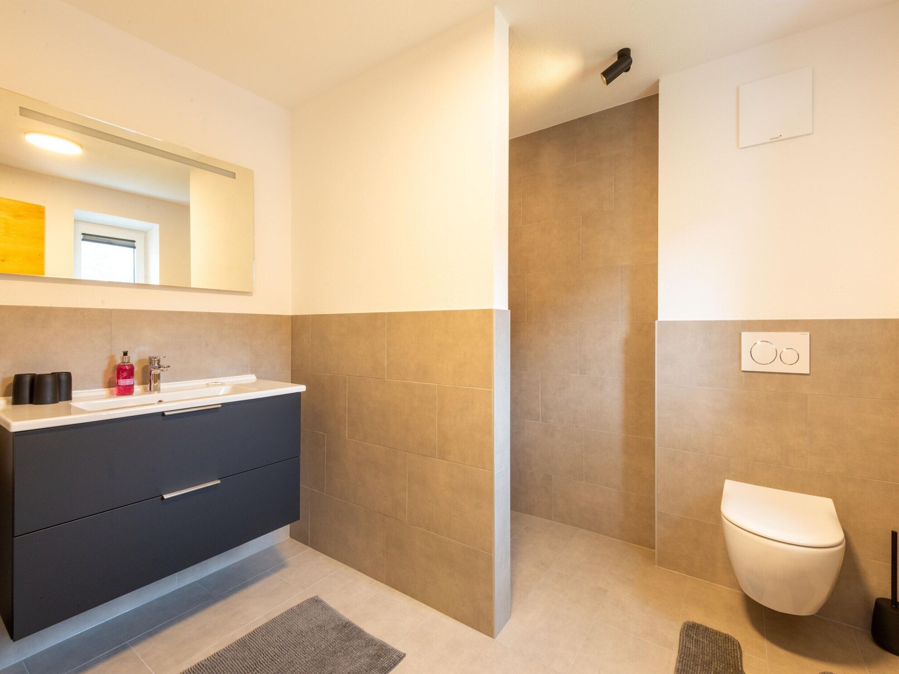 A modern bathroom with a dark grey vanity, a white toilet, and a shower area.