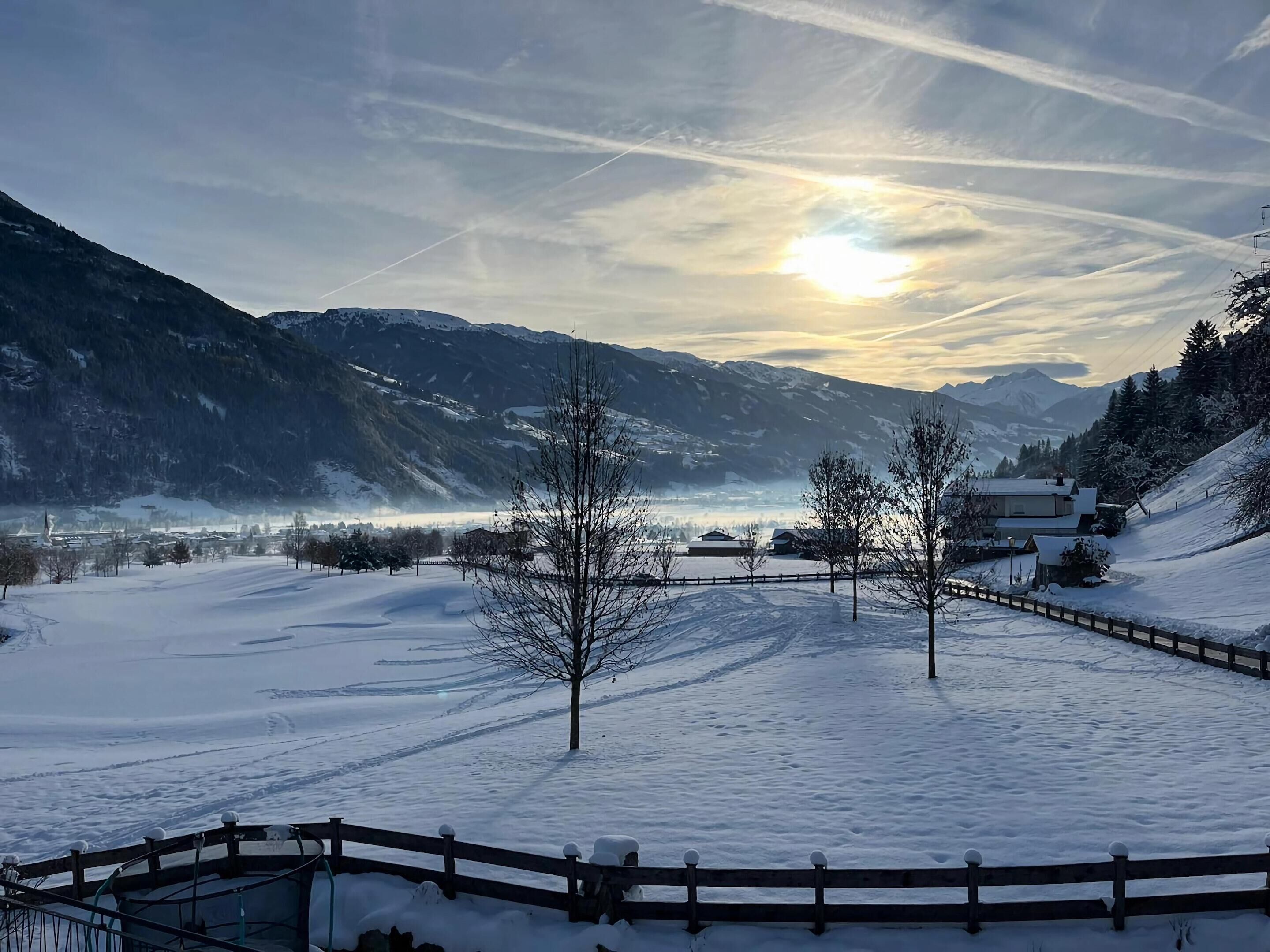 A snow-covered landscape with a wooden fence, a clear sky, and distant mountains.
