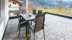 A covered patio with a table and chairs, a view of a mountain landscape, and a building labeled "green apartment" in the background. - Apartment in Uderns Near Spieljoch Ski (Uderns)