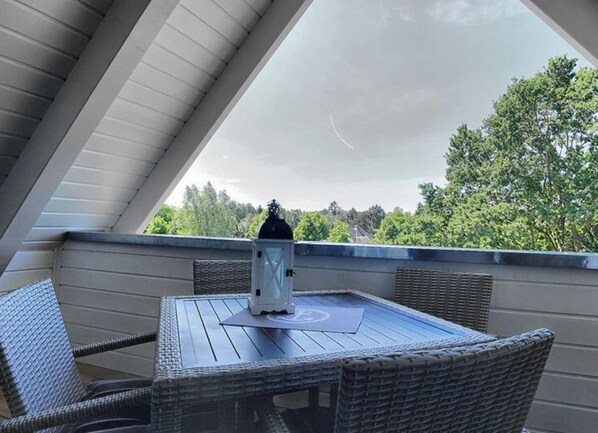 En möblerad uteplats med tak, bestående av ett bord och stolar, en lykta och utsikt över träd och himmel.