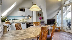 Eine moderne Küche mit weißen Schränken, einem Holztisch und einem großen Fenster mit Blick auf eine Terrasse.