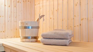 Uma sauna de madeira com um balde de metal e toalhas sobre um banco de madeira.