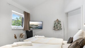 Quarto moderno com cama, televisão, janela com cortinas e vista para o verde.