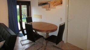 A dining area with a round wooden table, four black chairs, and a view of the outdoors through a glass door. - Schmitz 2 Comfortable Holiday Residence (De Haan)